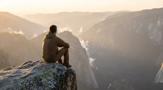 Personne assise sur un rocher contemplant un paysage montagneux dans une lumière dorée