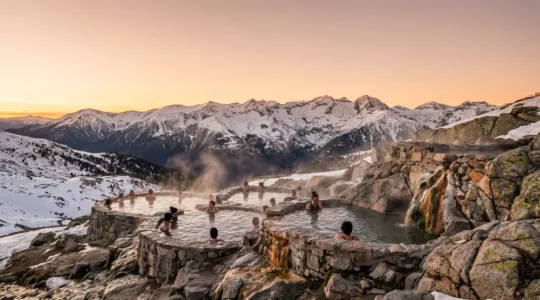 Baigneurs profitant d'un bassin d'eau chaude naturelle dans un amphithéâtre de pierre avec vue panoramique sur les sommets enneigés des Pyrénées