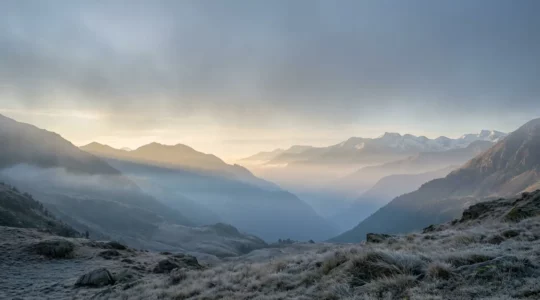 Vallée pyrénéenne isolée baignée dans la brume matinale avec sommets enneigés au loin